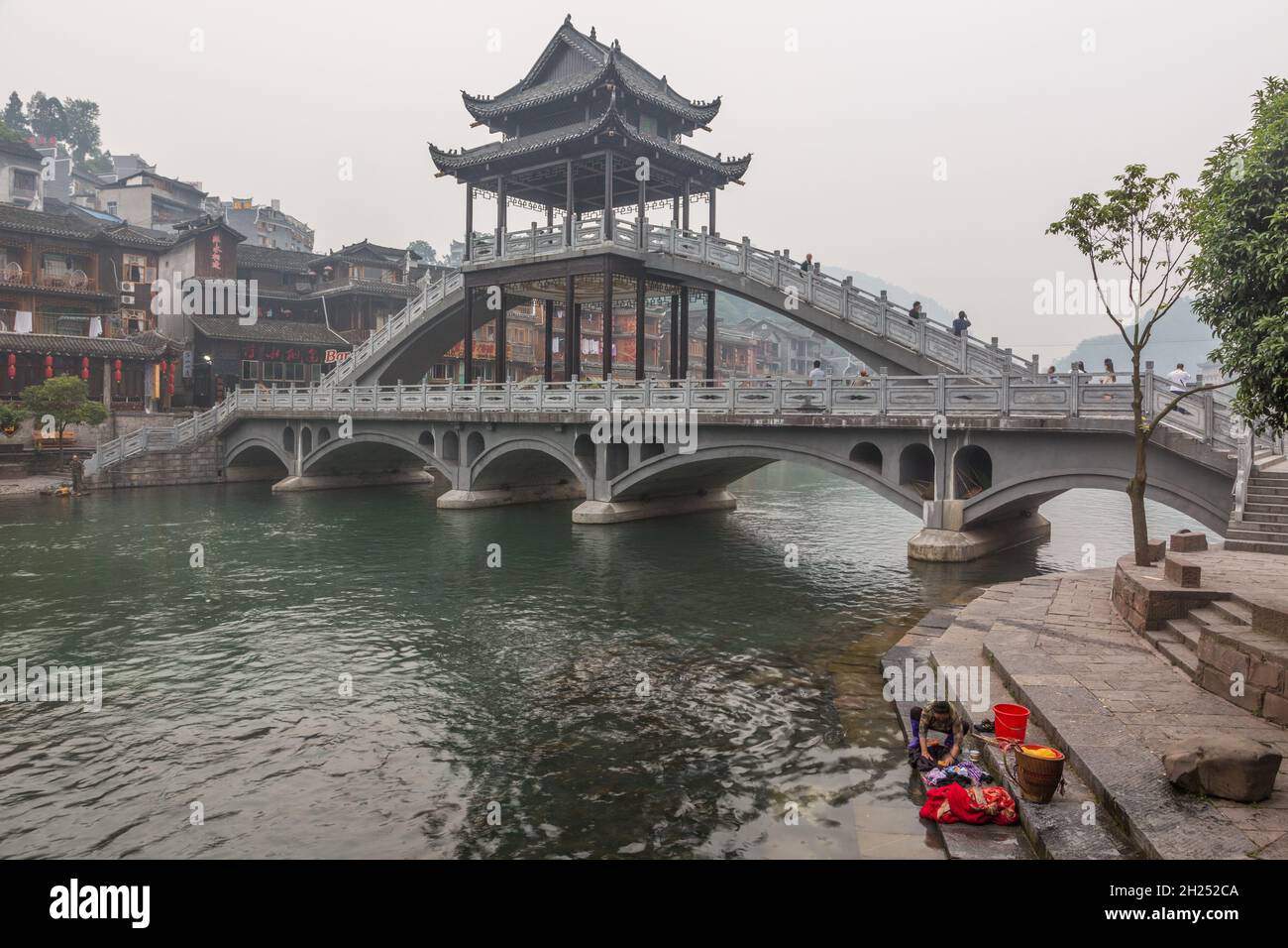 A woman does laundry in the Tuojiang River in front of the Fenghuang Bridge. Fenghuang, China. Stock Photo