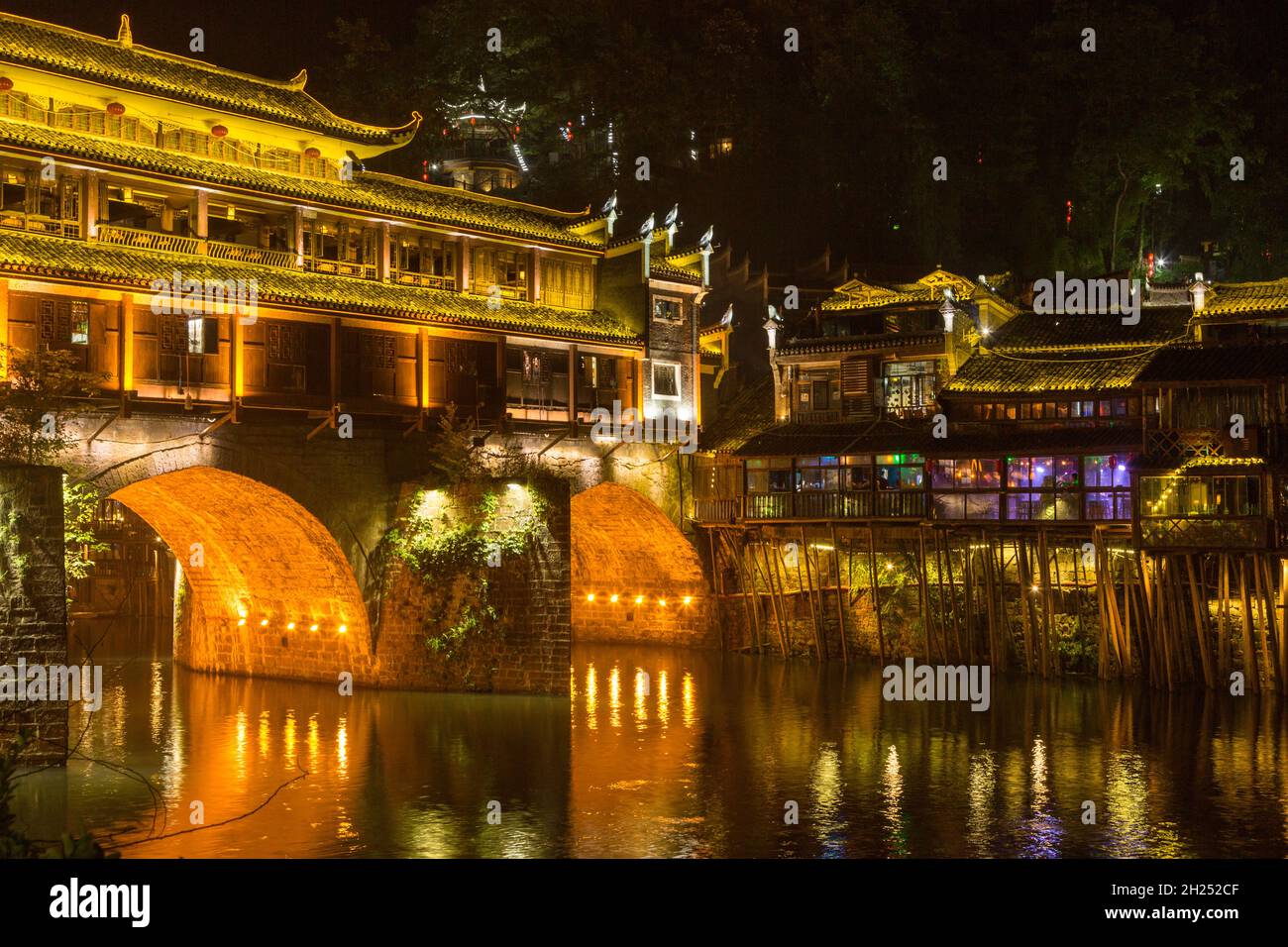 Diaojiao-style buildings on stilts next to the Phoenix Hong Bridge at night.  Fenghuang, China. Stock Photo
