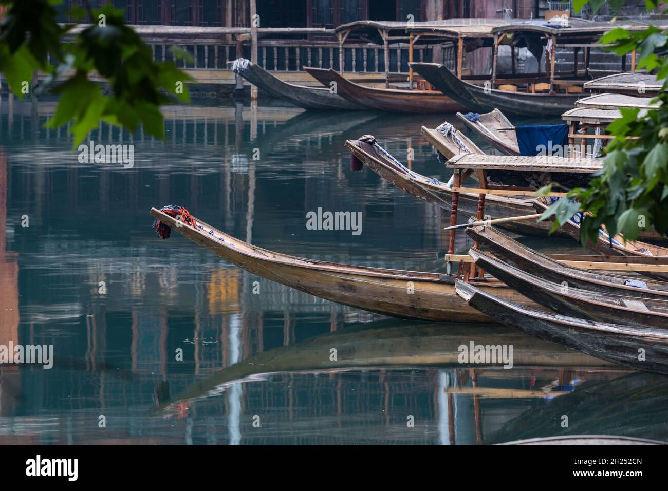 Covered tour boats reflected in the calm water of the Tuojiang River in Fenghuang, China. Stock Photo