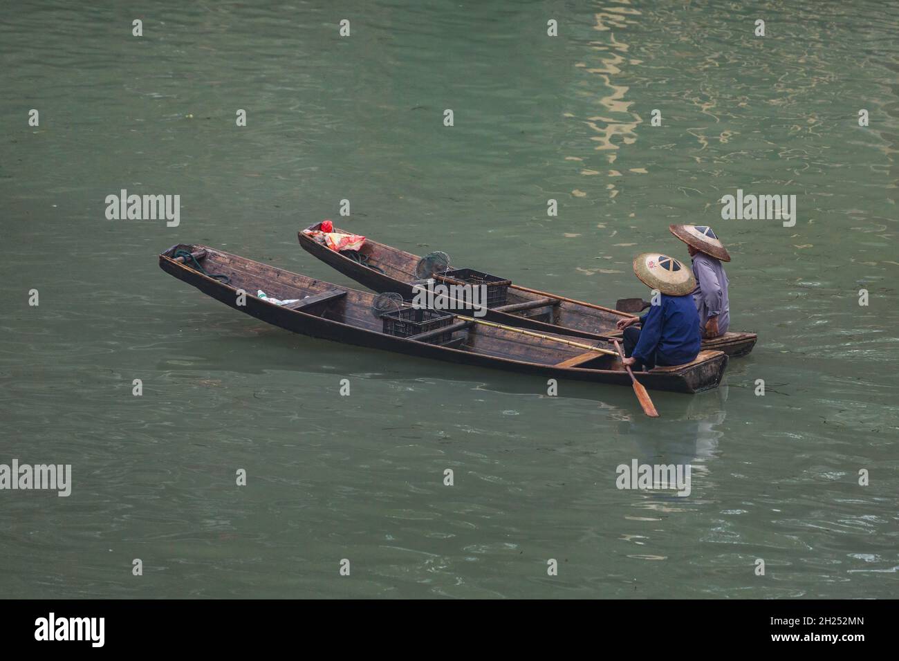 Two men in a traditional conical has paddle sampans on the Tuojiang River in Fenghuang, China. Stock Photo