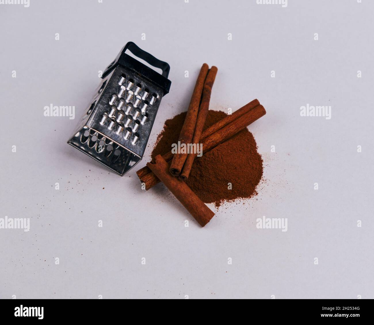 https://c8.alamy.com/comp/2H2534G/a-small-grater-with-cinnamon-sticks-and-powder-isolated-on-a-white-background-2H2534G.jpg