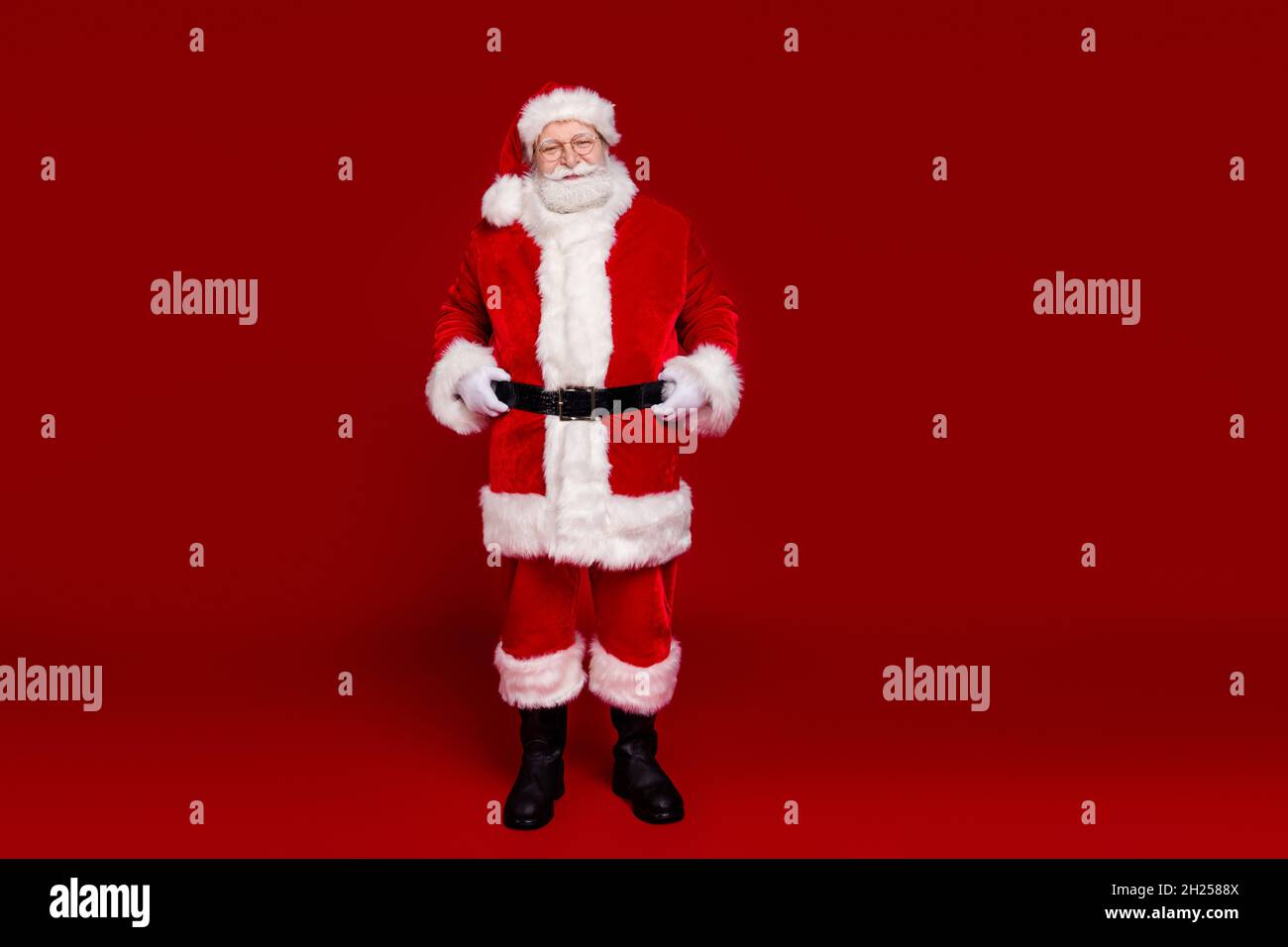 Photo of cheerful cute man pensioner dressed santa claus costume boots belt walking empty space smiling isolated red color background Stock Photo