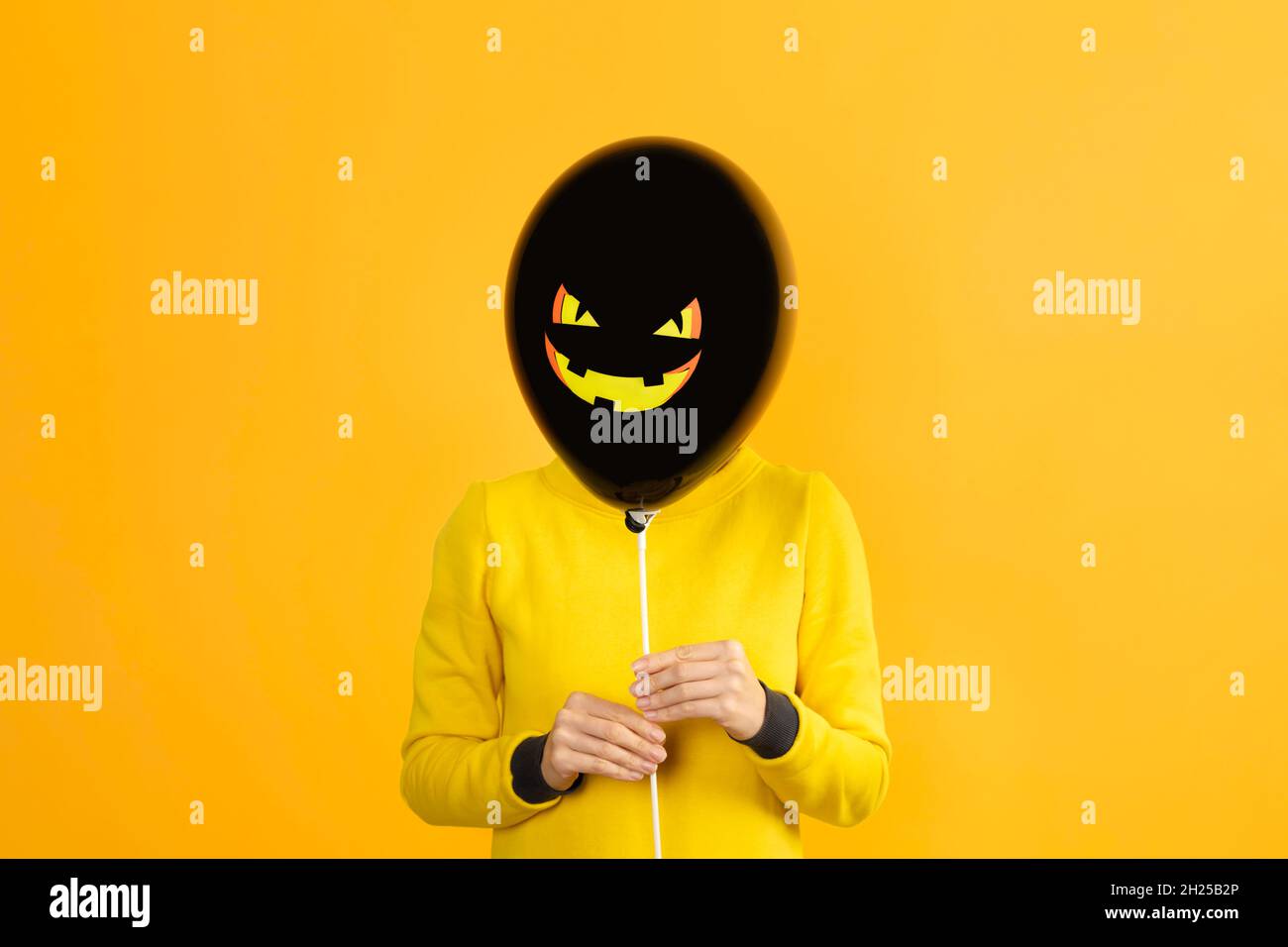 Halloween concept. Girl holding black balloon with Jack lantern or scary pumpkin face isolated on yellow background Stock Photo