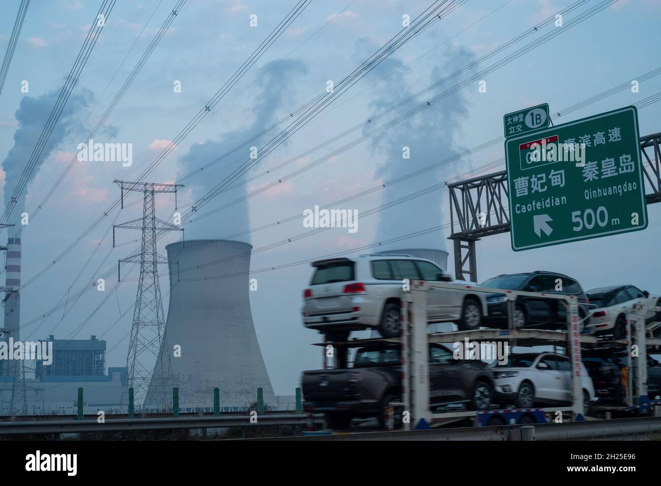 A flatbed truck carrying new cars passes by a power plant in Tianjin, China. 19-Oct-2021 Stock Photo