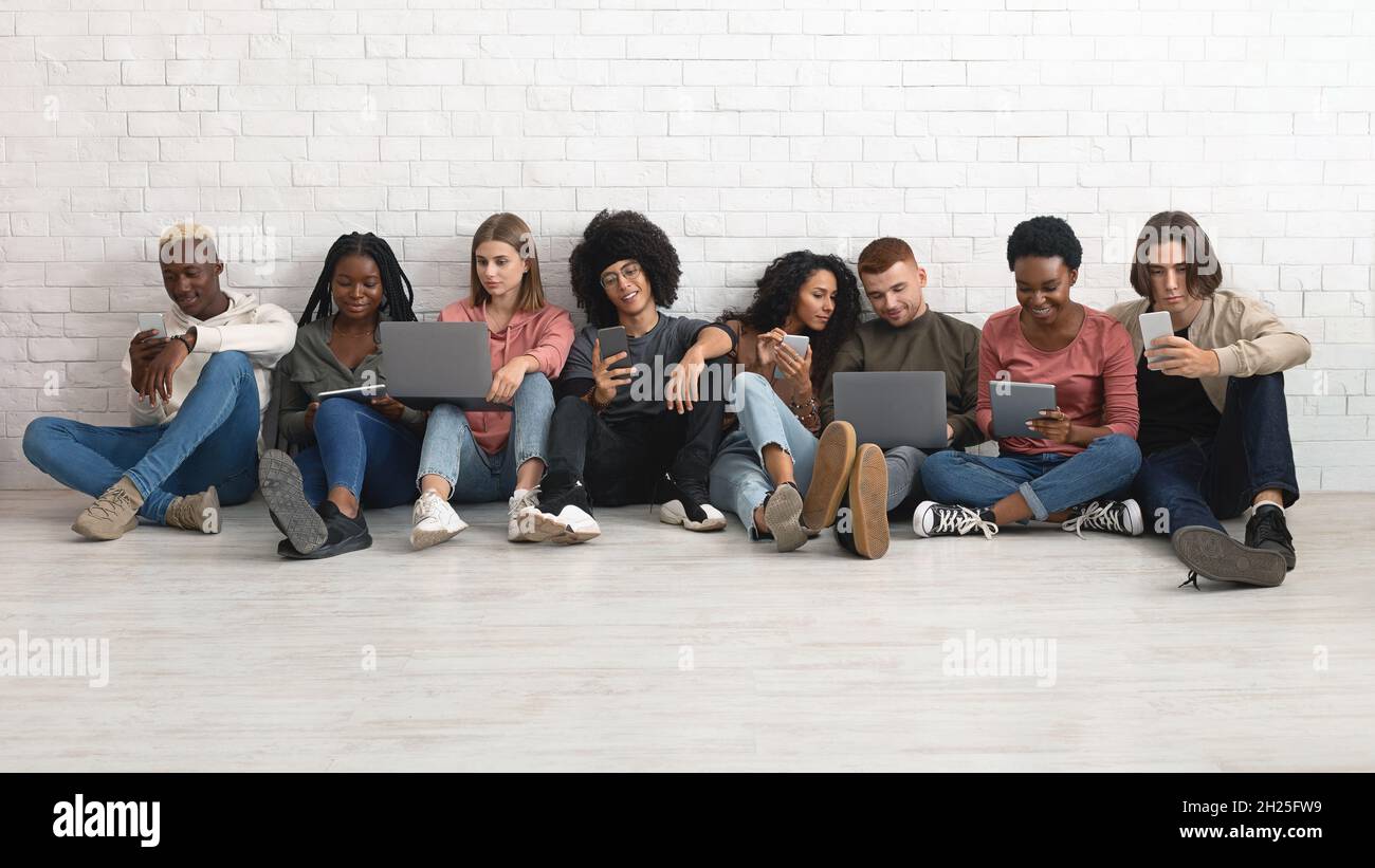 Happy multiethnic millennials using gadgets while spending time together Stock Photo
