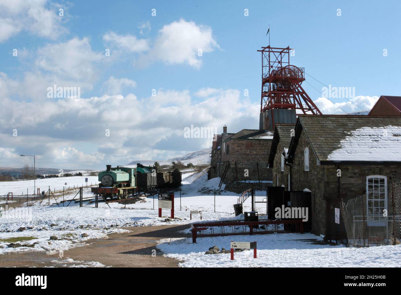 Big Pit, mining museum steam train & wagons winding gear buildings blue sky fluffy white clouds winter snow Blaenafon Wales UK copy space Stock Photo