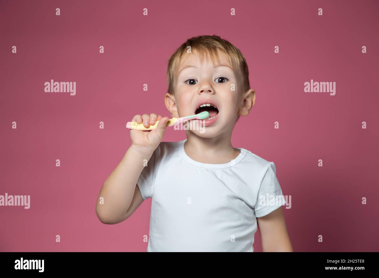 Smiling caucasian little boy cleaning his teeth with manual children toothbrush on pink background. Stock Photo