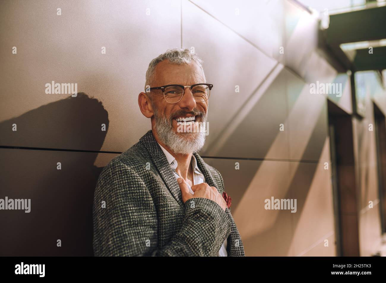 High-spirited bespectacled male leaning against the building wall Stock Photo