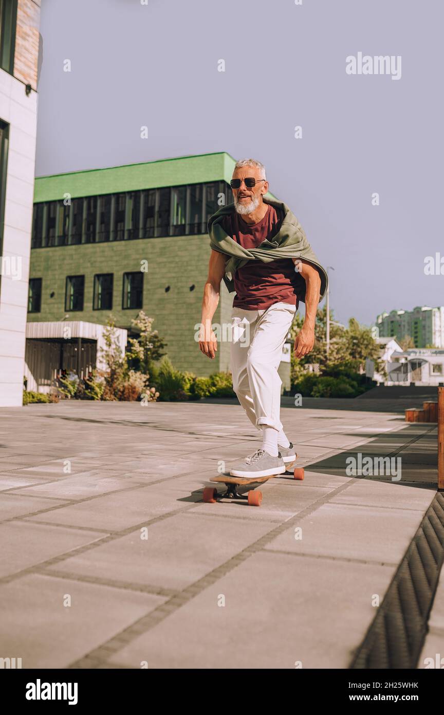 Gray-haired bearded man skateboarding in the street Stock Photo