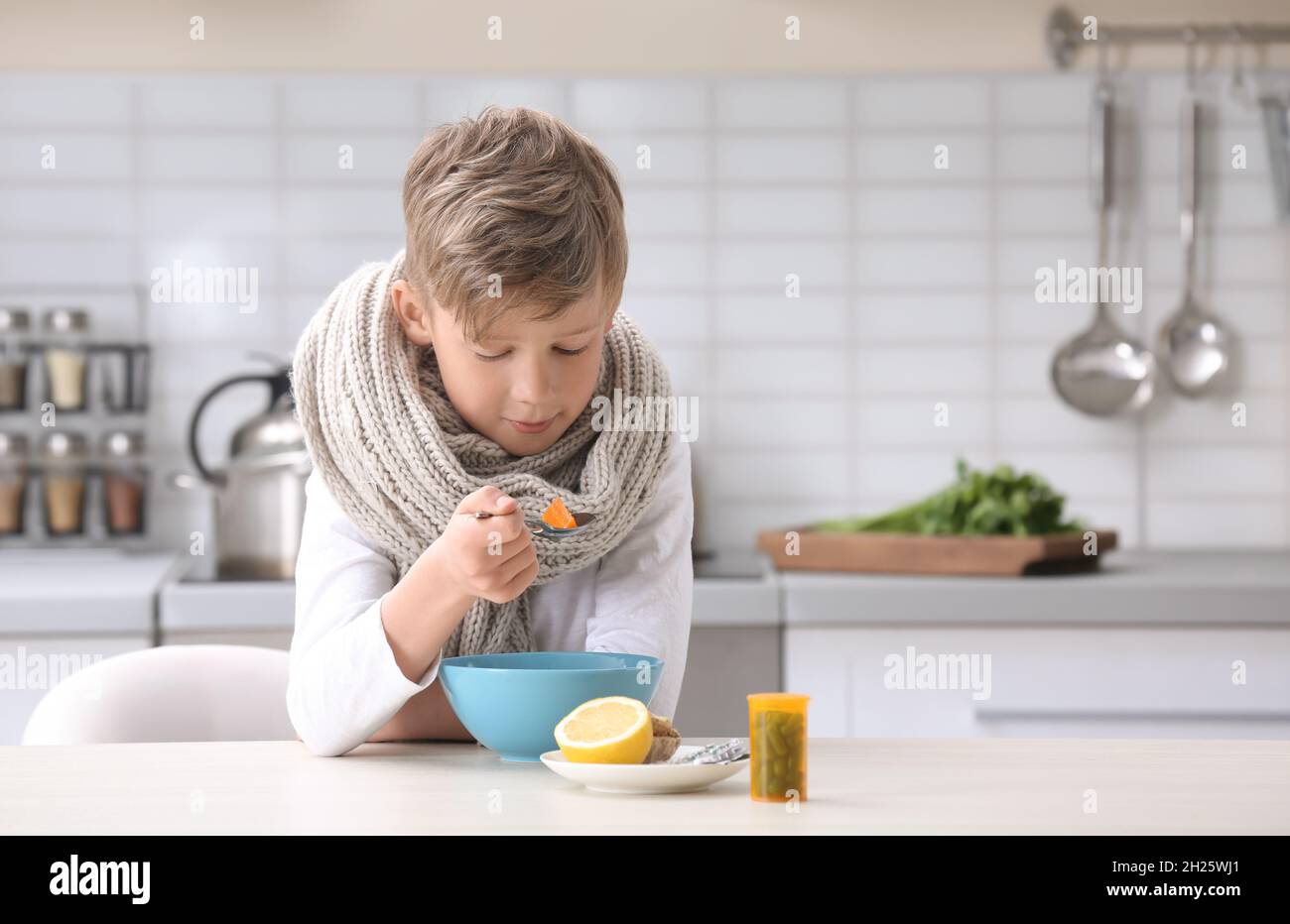 Sick little boy eating broth to cure cold at table in kitchen Stock