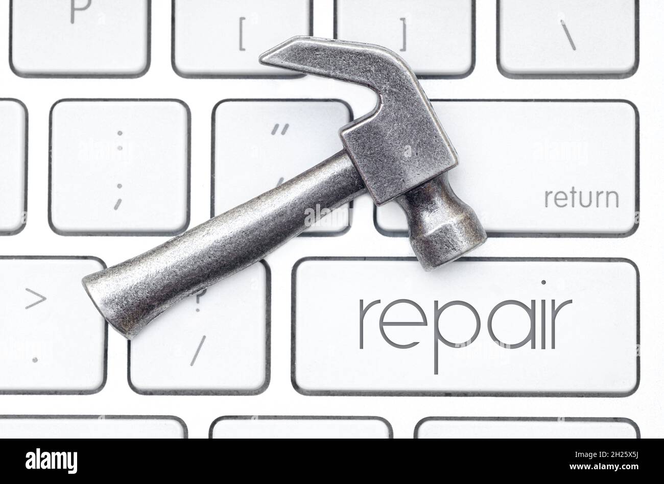 Small steel hammer lies on the keyboard, which has a key labeled as REPAIR. Hardware service concept. Stock Photo