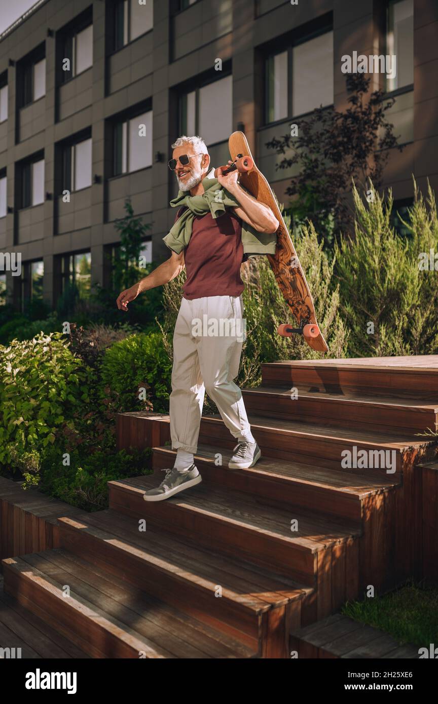 Cheerful skateboarder in sunglasses going down the wooden stairs Stock Photo