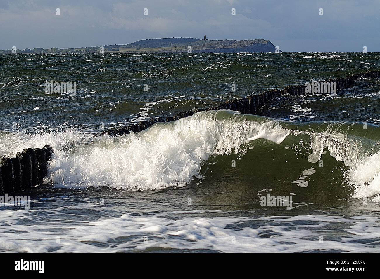 Breakwater and wave with Hiddensee in background. Stock Photo