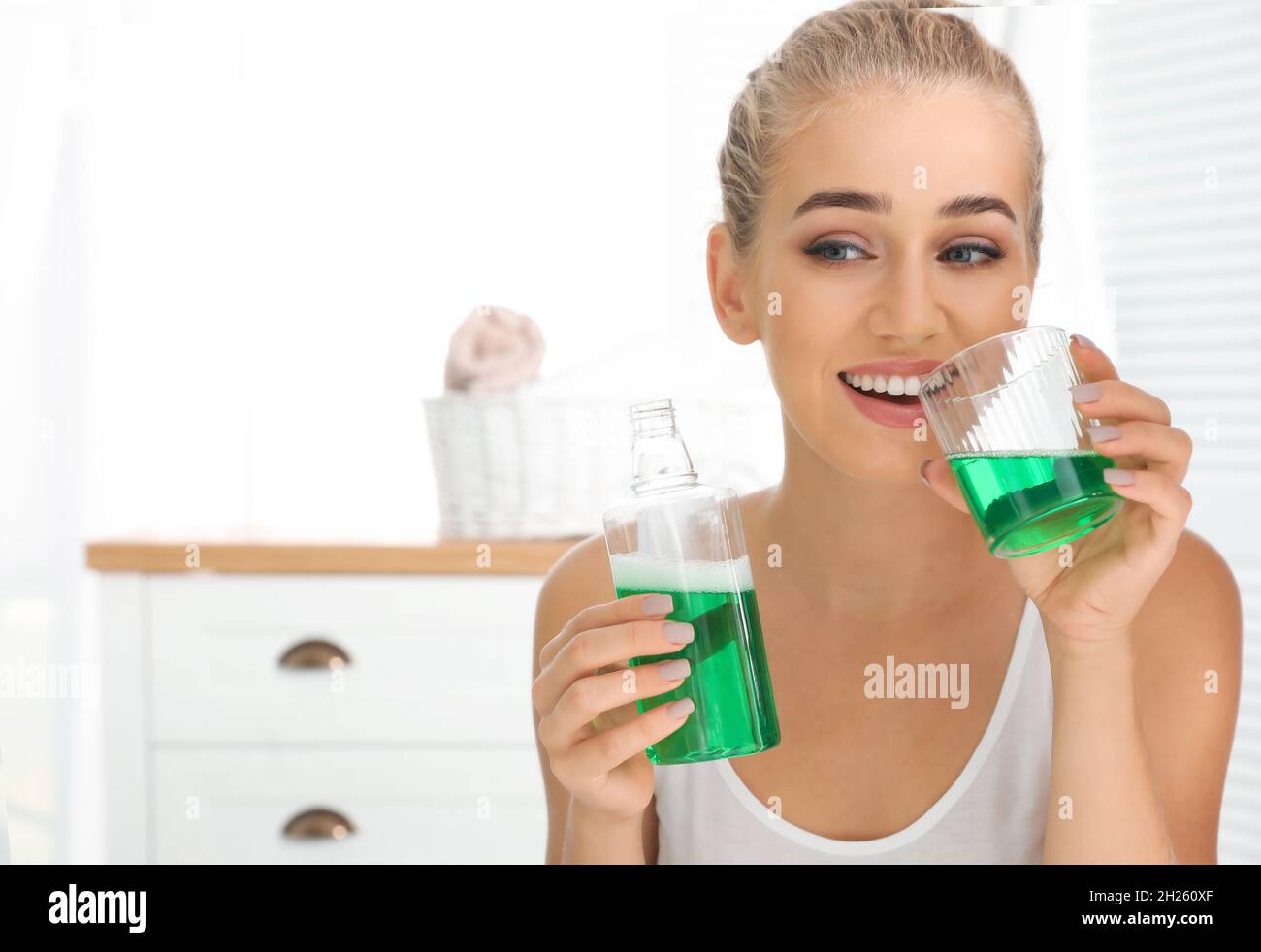 Woman holding bottle and glass with mouthwash in bathroom. Teeth care