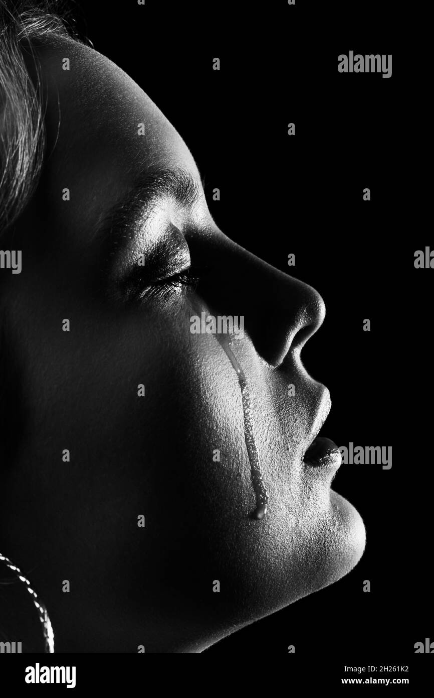 sad woman with closed eyes crying, on black background, closeup portrait, profile view, monochrome Stock Photo