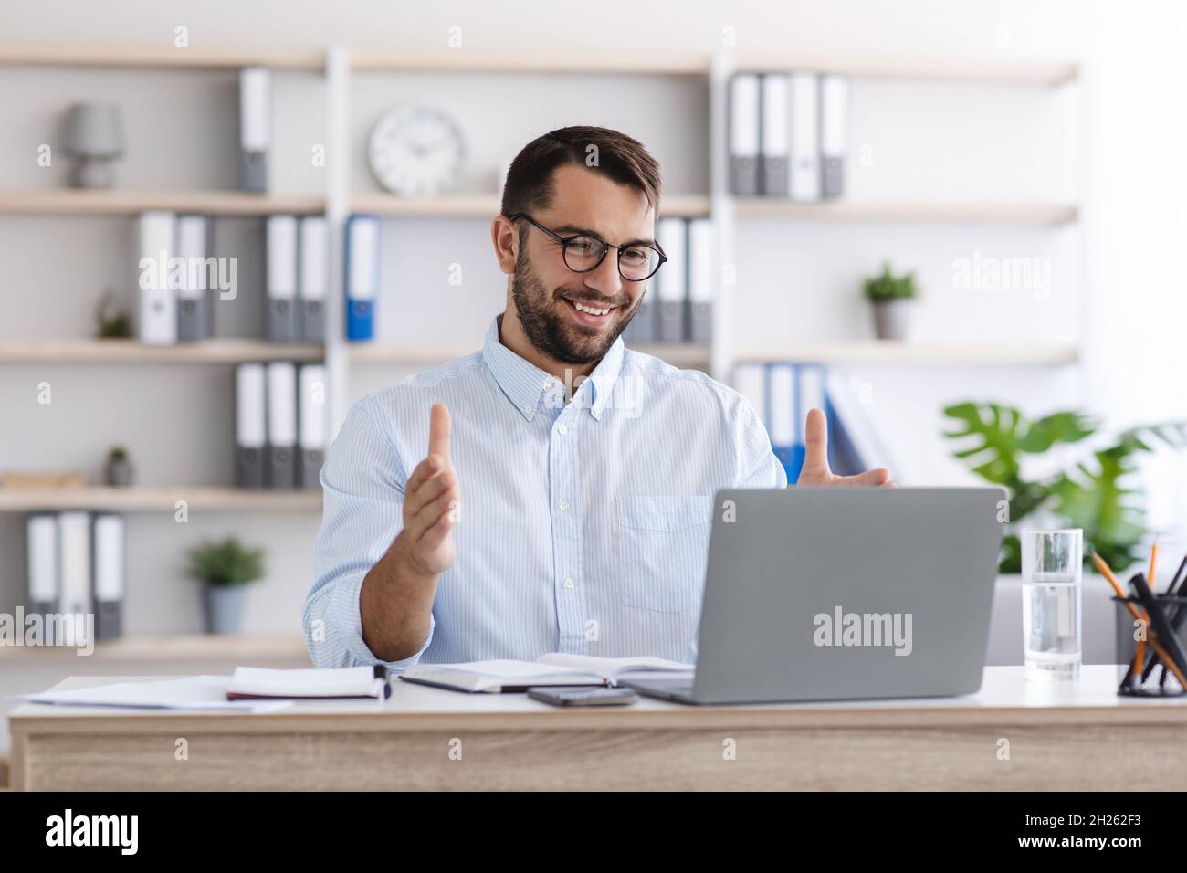 Happy mature caucasian guy with beard in glasses work at laptop, making video call and gesturing Stock Photo
