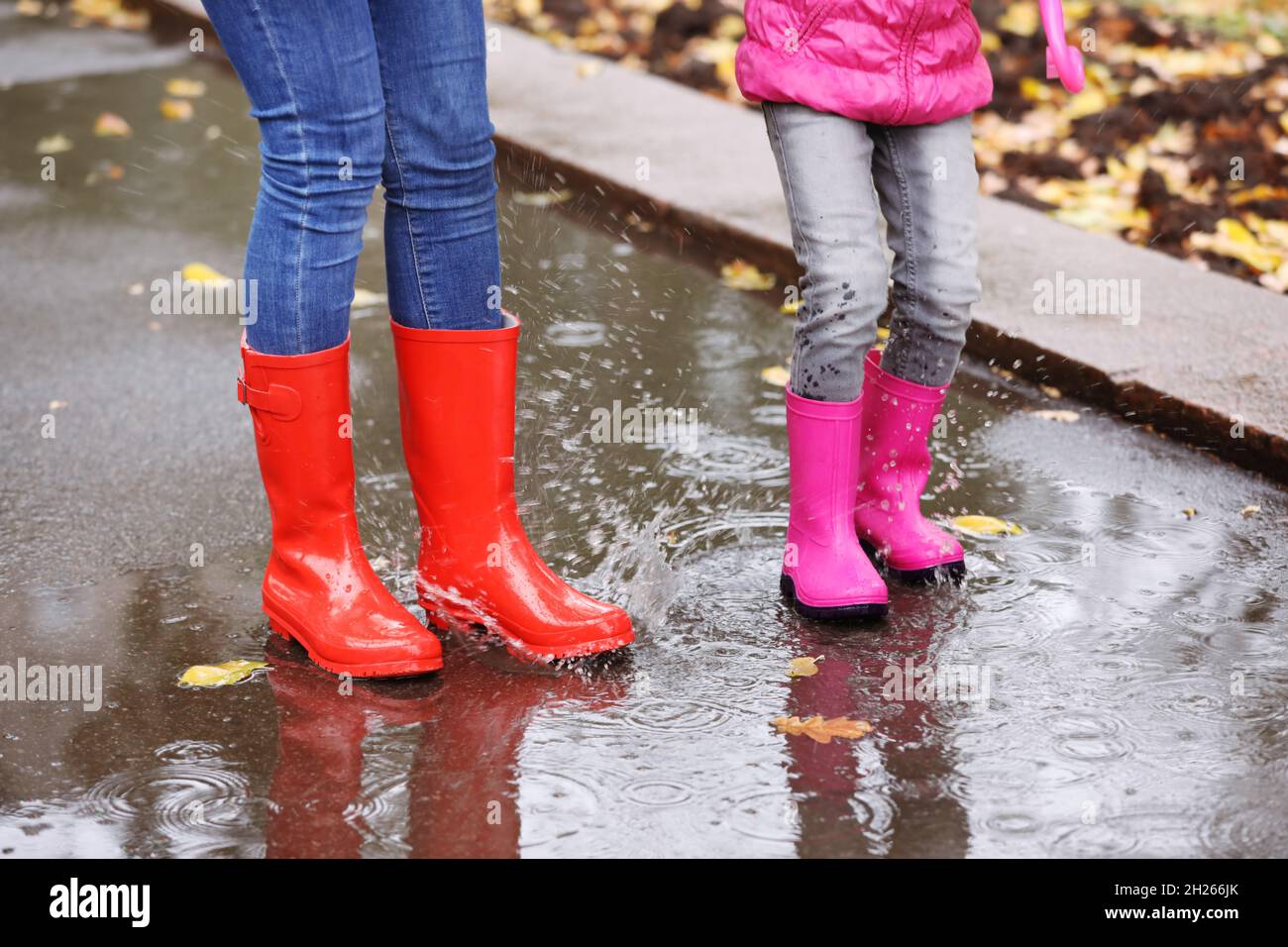 Mother and daughter wearing rubber boots splashing in puddle on rainy ...