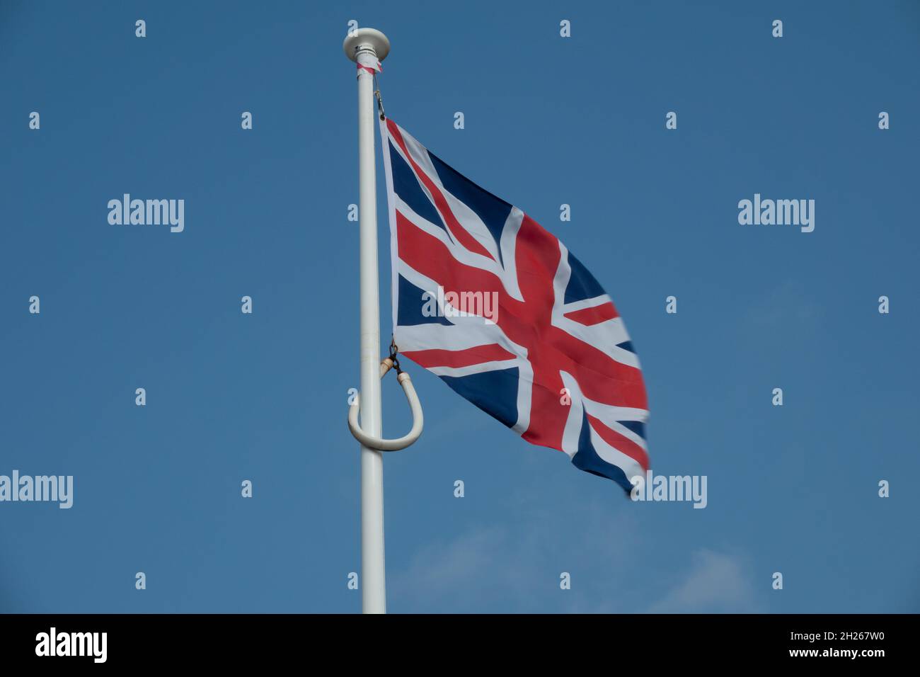 A union jack flag flying from a white flag pole against a blue sky Stock Photo