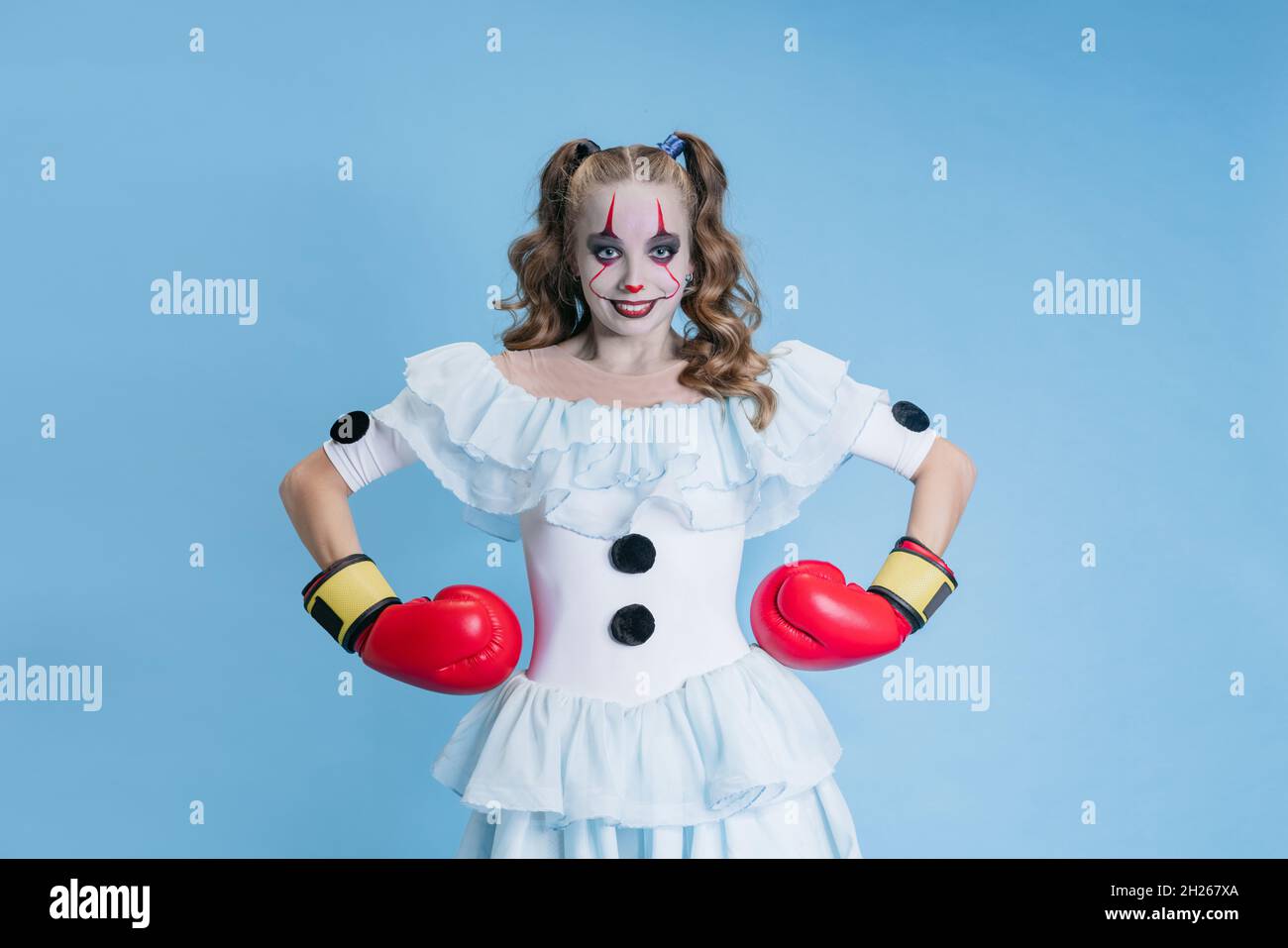 Portrait of charismatic young girl in Halloween costume of movie character with spooky facial expression isolated over blue background Stock Photo