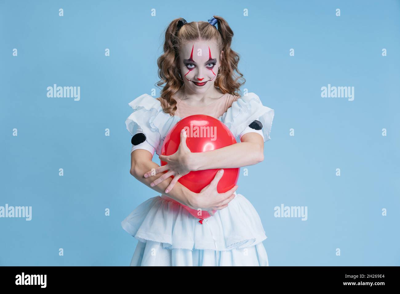 Conceptual portrait of charming young girl in Halloween costume of movie character with spooky facial expression isolated over blue background Stock Photo