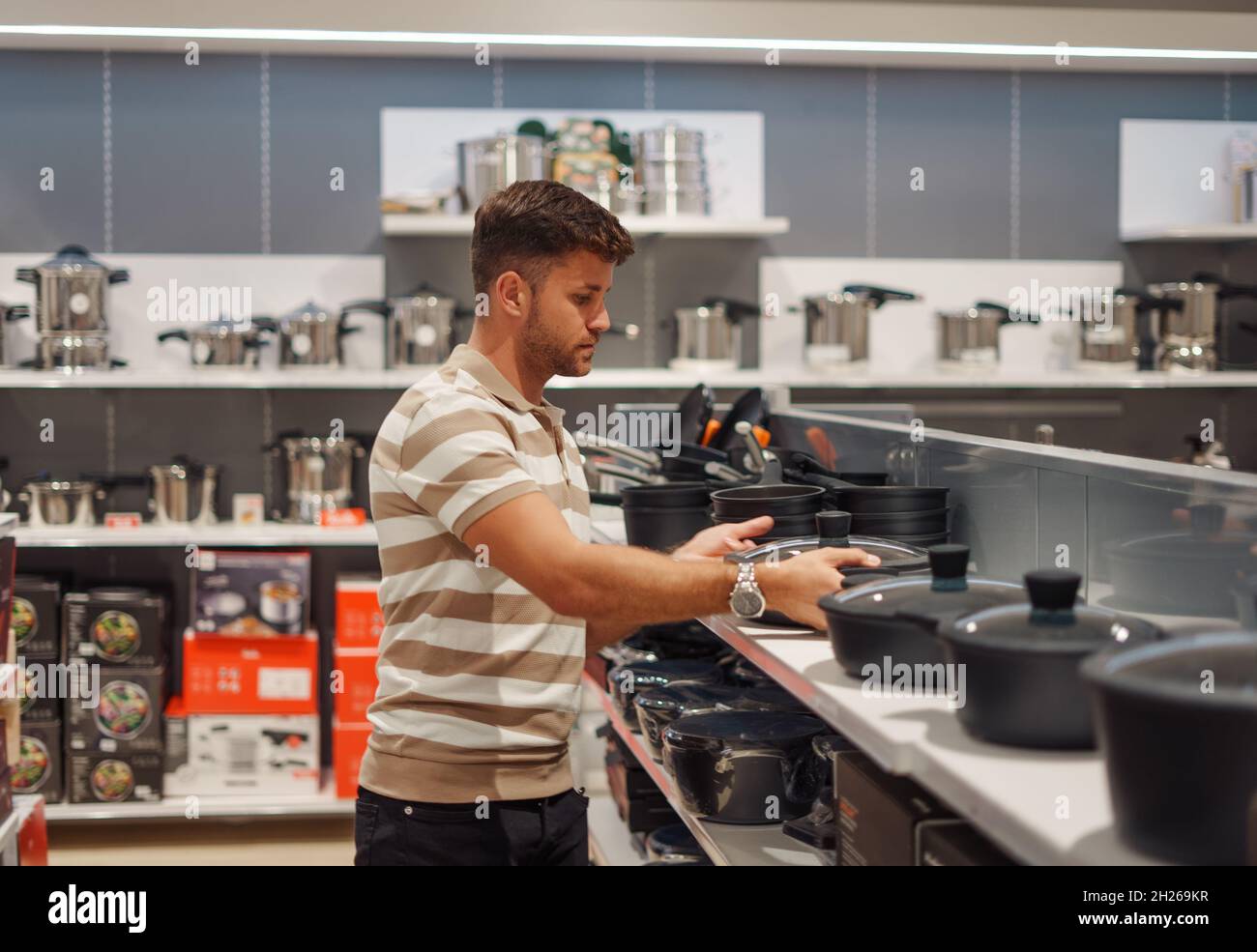 Male customer in casual clothes examining cooking pot on shelf while buying cookware in modern mall Stock Photo