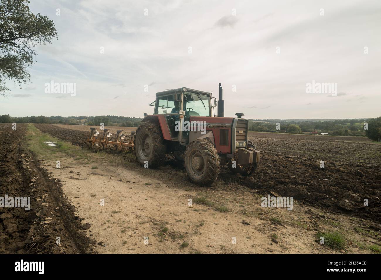 Ploughing large field of sandy sticky clay soil loam by old tractor turning the soil before sowing seed or planting in Kent Stock Photo
