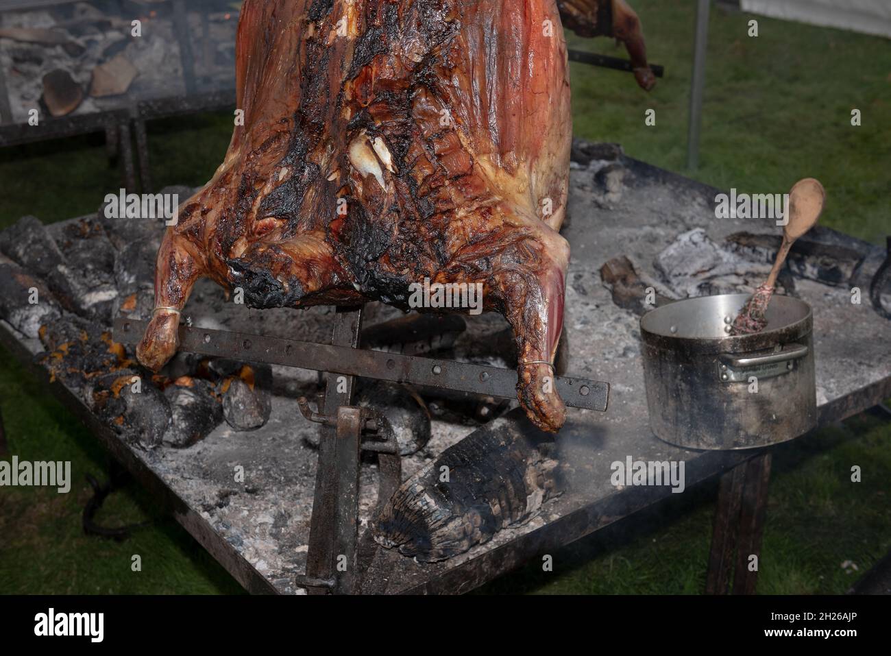 Smoke impregnated aromas infuse into the oils and meat of a barbecued sheep over an open wood and charcoal fire Stock Photo