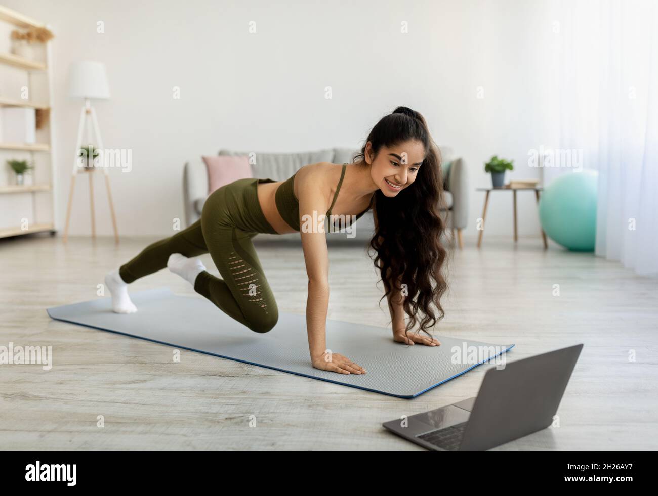 Effective strength exercises. Indian woman working out to online video tutorial, running with her hands on floor at home Stock Photo