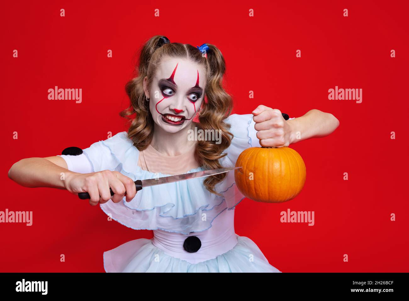 Halloween spooky theme. Mystical blonde girl with bright holiday make up holding knife isolated over red background Stock Photo