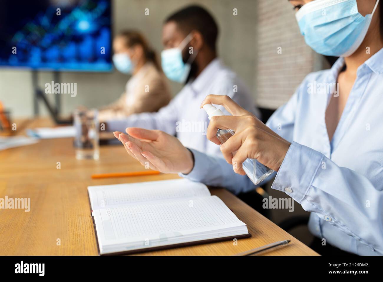 Female Employee In Face Mask Applying Disinfectant Spray On Hands In Office Stock Photo