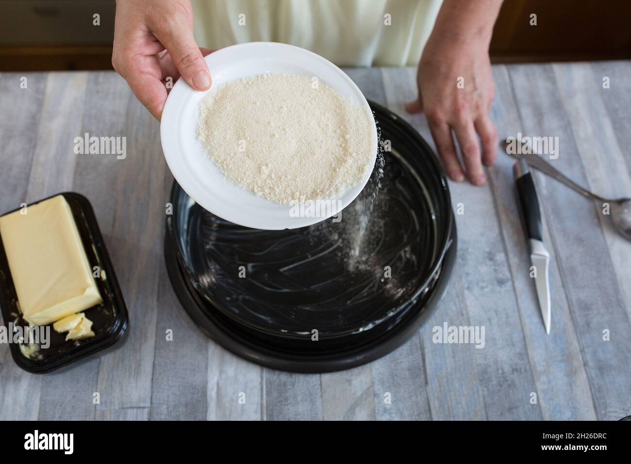 A step-by-step process for making a sour cream chocolate cake. Women's hands prepare a baking dish, grease with butter and sprinkle with semolina. Bak Stock Photo