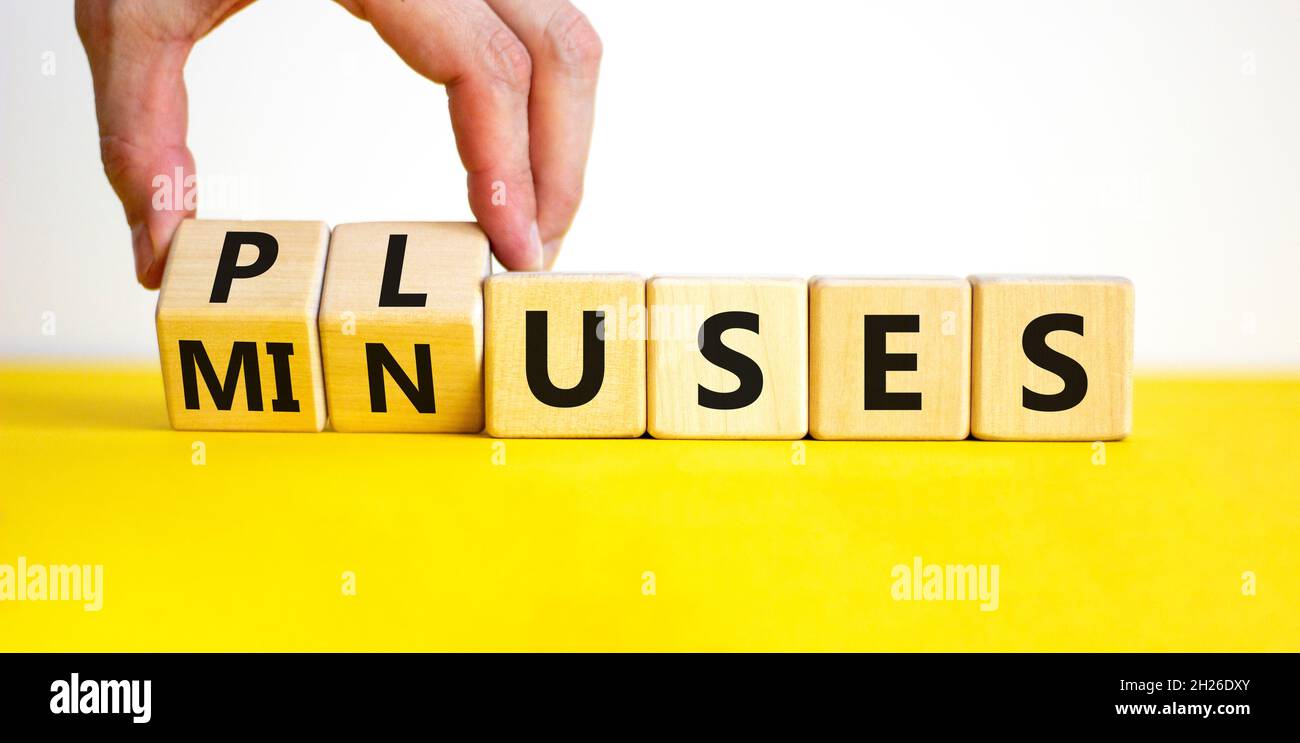 Pluses and minuses symbol. Businessman turns wooden cubes and changes the word 'minuses' to 'pluses'. Beautiful yellow table, white background. Busine Stock Photo