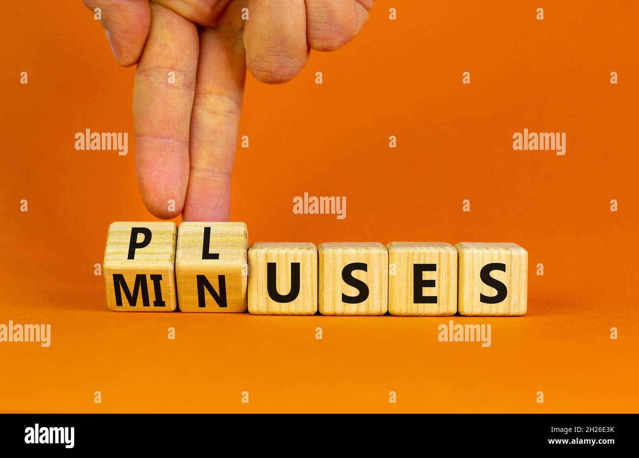 Pluses and minuses symbol. Businessman turns wooden cubes and changes the word 'minuses' to 'pluses'. Beautiful orange table, orange background. Busin Stock Photo