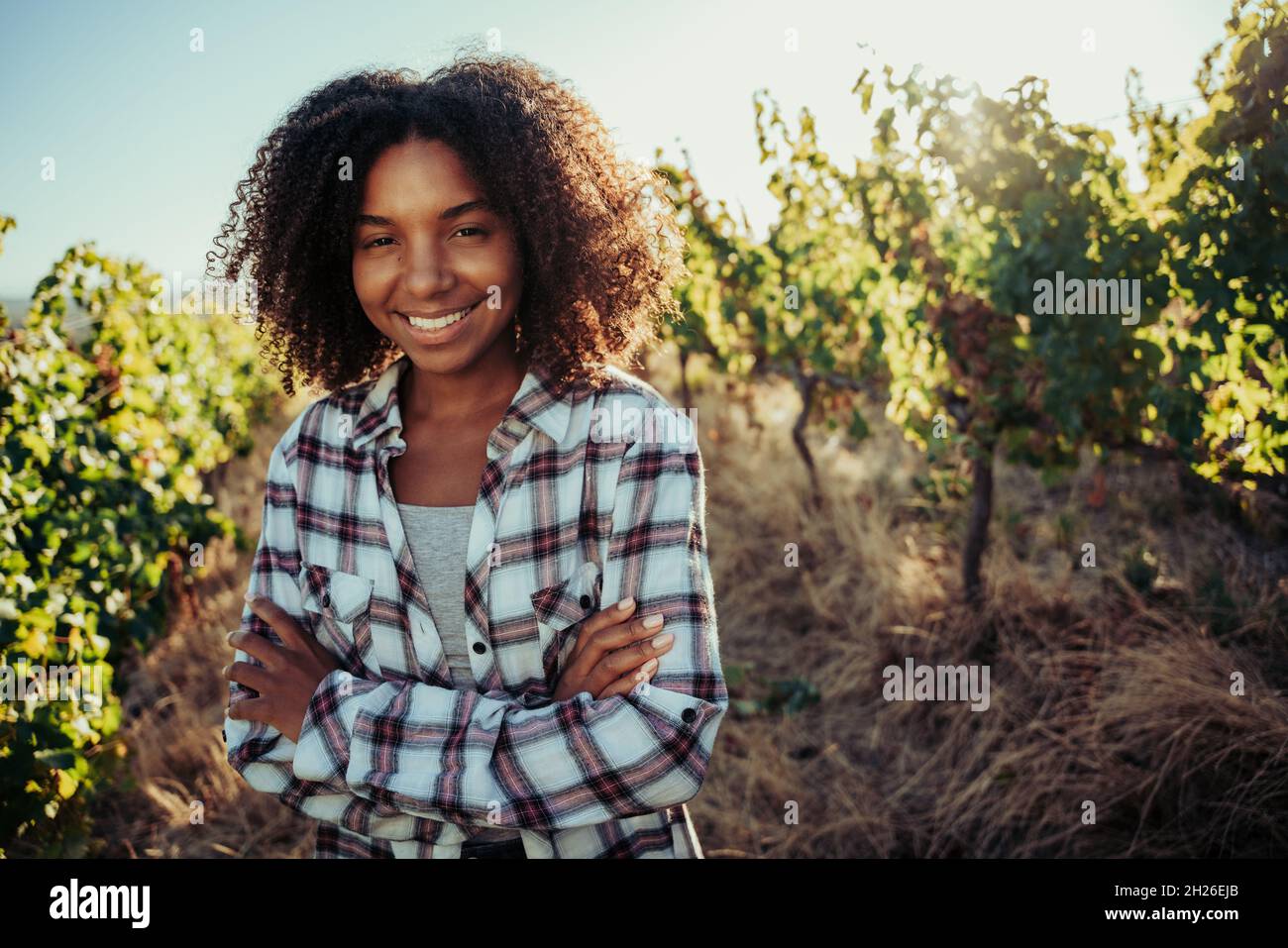 Mixed race female farmer standing with crossed arms smiling standing in beautiful vineyards Stock Photo