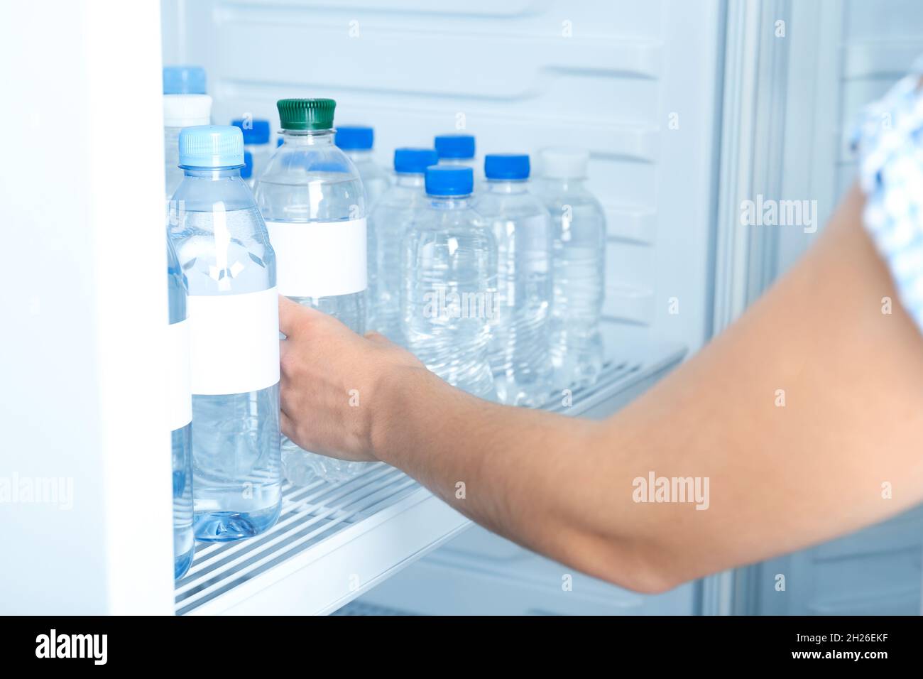 Woman taking bottle of water from refrigerator, closeup. Mockup for