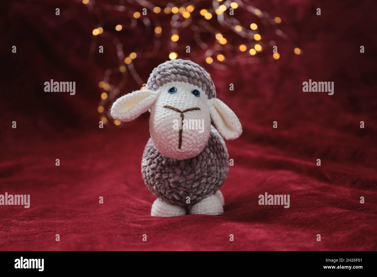 Cute plush ram for design of Christmas card. Gray and white handmade amigurumi sheep crocheted with blue eyes stands on red soft blanket against backg Stock Photo Alamy