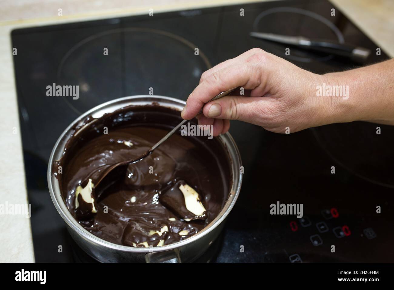 Step-by-step process for making a sour cream chocolate cake. The process of making chocolate glaze. Butter is added to the heated mixture of sour crea Stock Photo