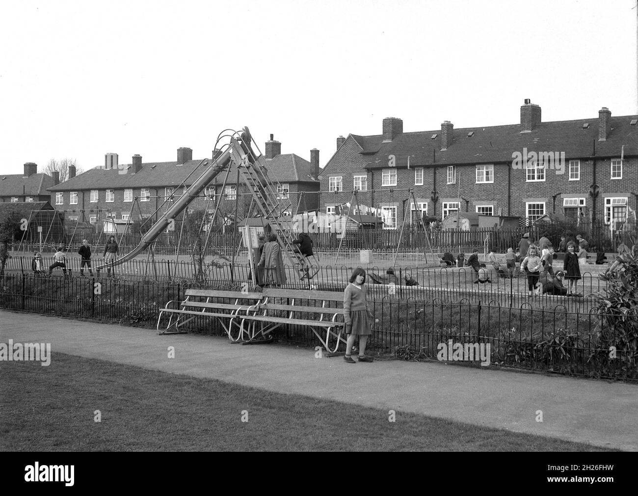 1950s, historical, in a public park, situated by a row of suburban council houses, England, UK, children playing in a traditional playground, with metal slide and sandpit. Stock Photo