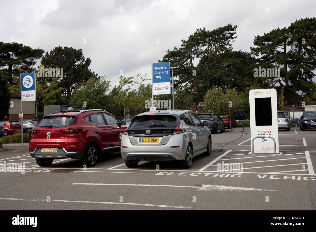 Nissan Leaf and MG EV charging at Pod Point electric vehicle charging point sponsored by VW  Tesco Churchdown UK Stock Photo