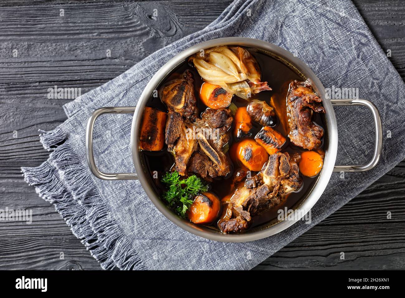 beef broth of beef meat on bones slow cooked with charred vegetables: carrot, onion, garlic, and spices served in a pot on a wooden table, top view, f Stock Photo