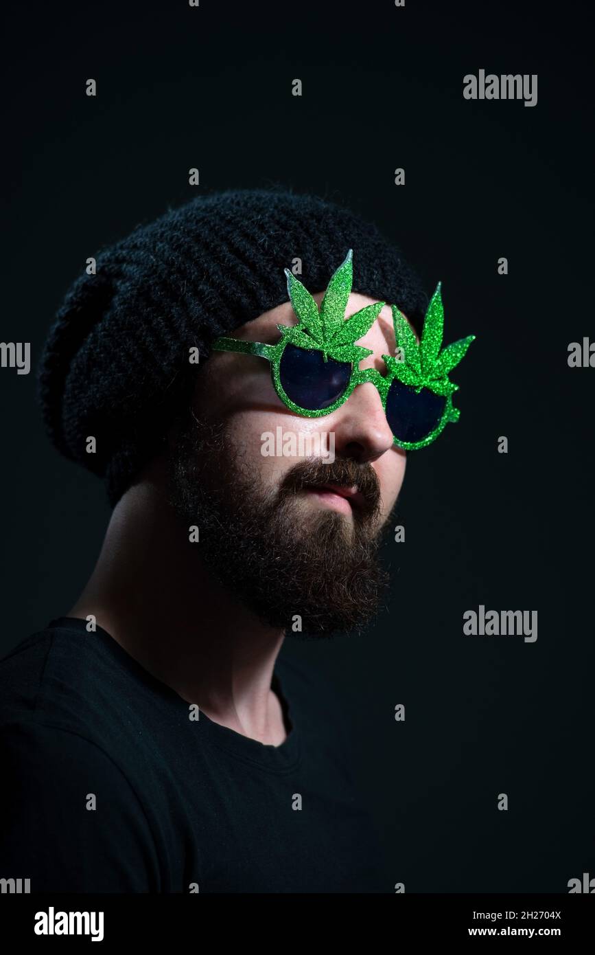authentic portrait of a cheerful guy in sunglasses marijuana, on a dark background Stock Photo