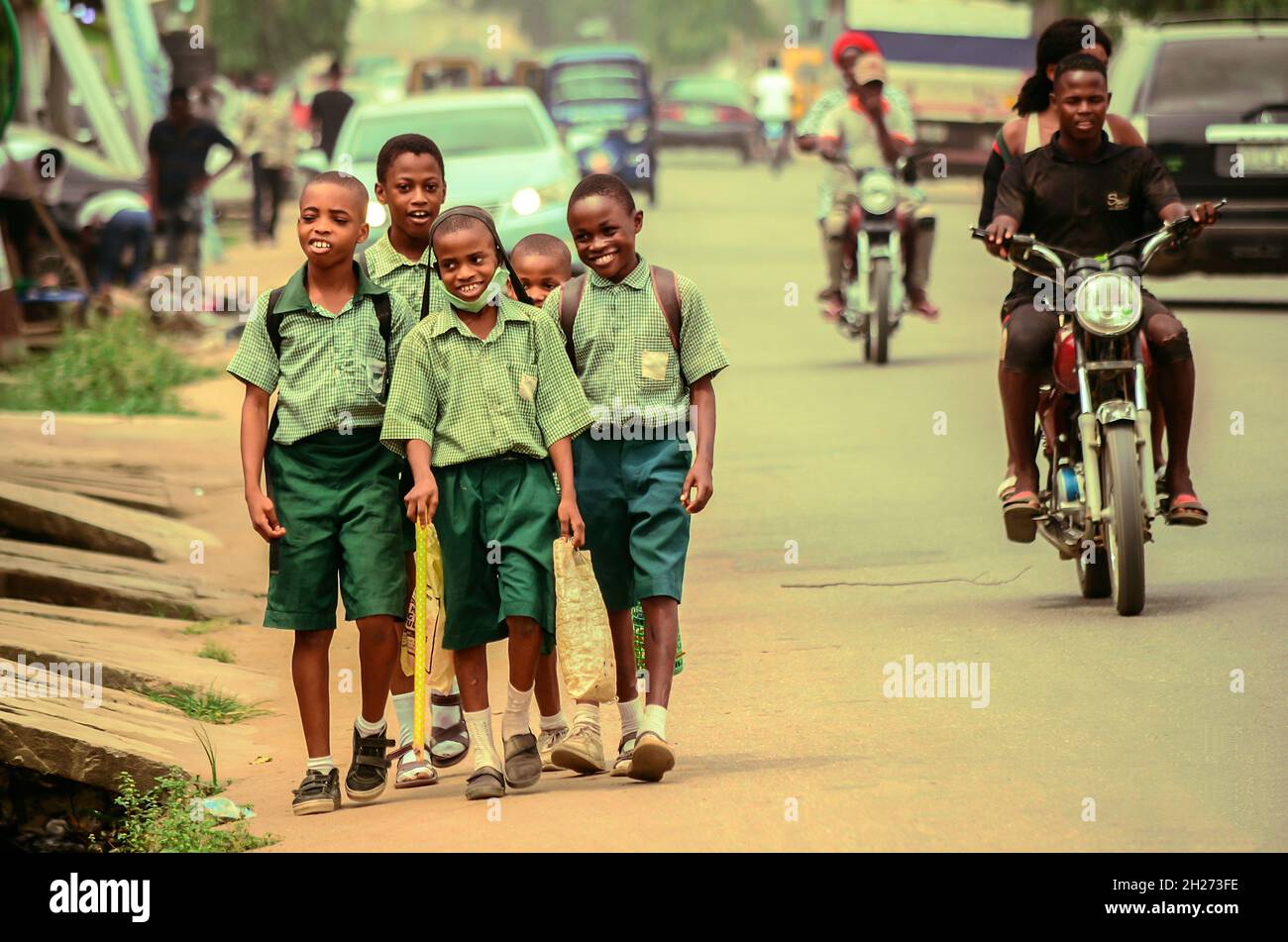 Front view of a diverse group of school children heading home along a road together in the sun, carrying their schoolbags and talking to each other. Stock Photo
