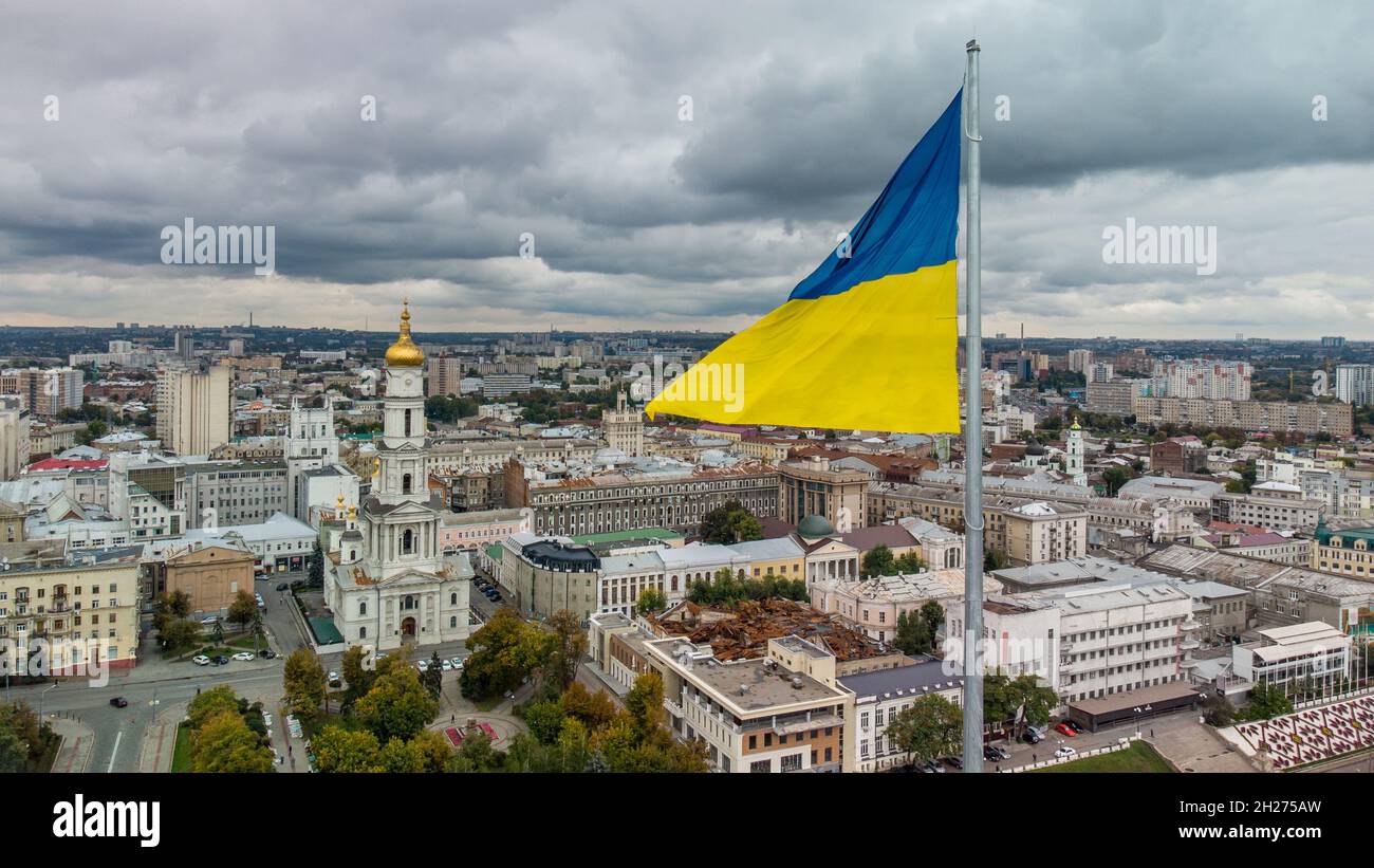 Bright flag of Ukraine waving close-up with autumnal epic gray cloudscape, city panoramic aerial view near river Lopan embankment, Dormition Cathedral Stock Photo