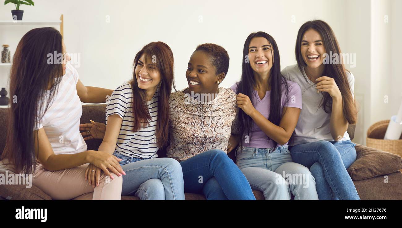 Diverse group of happy young women sitting on couch, talking and having fun together Stock Photo
