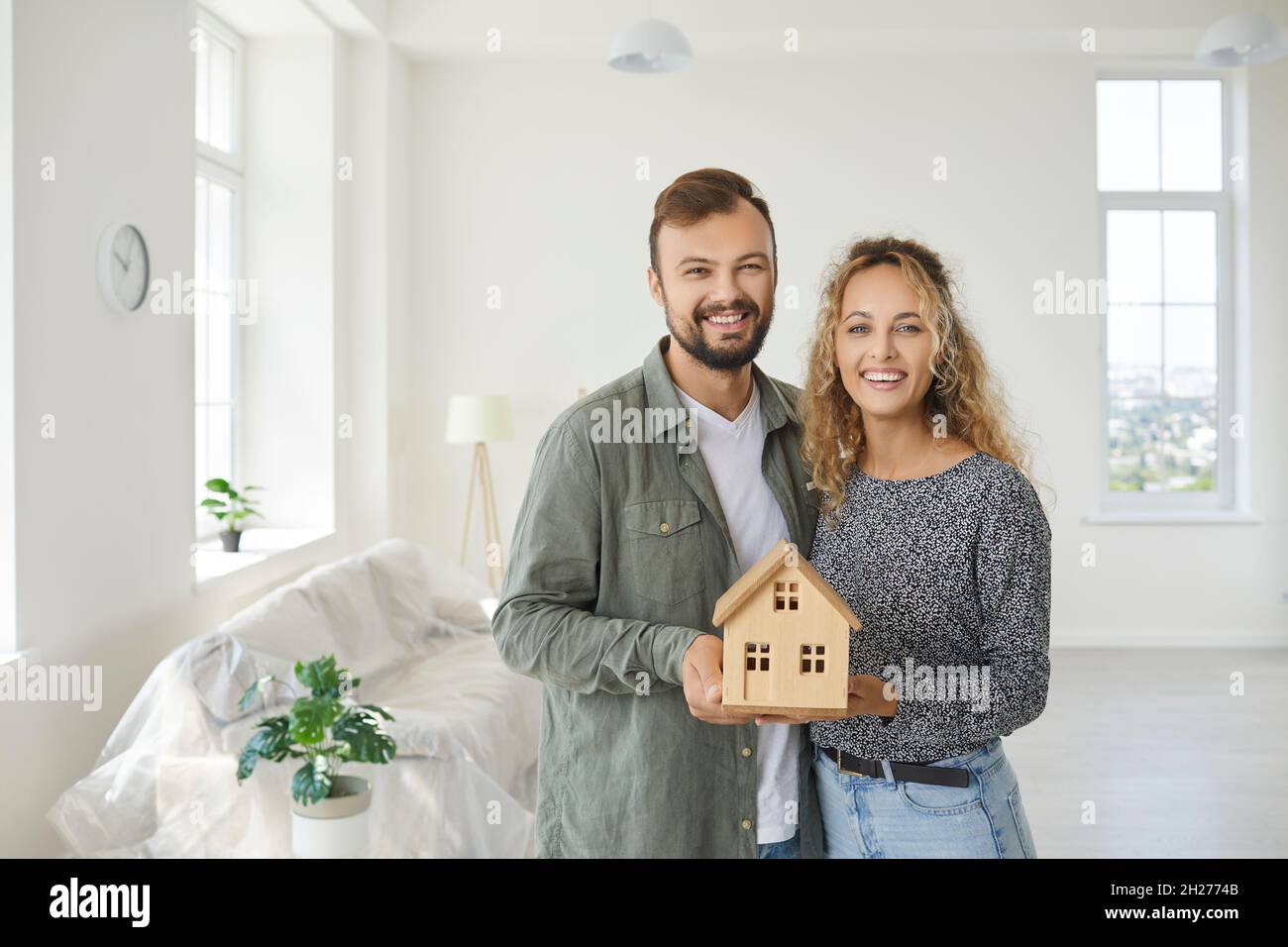 Happy young couple standing in their new home and holding a miniature ...
