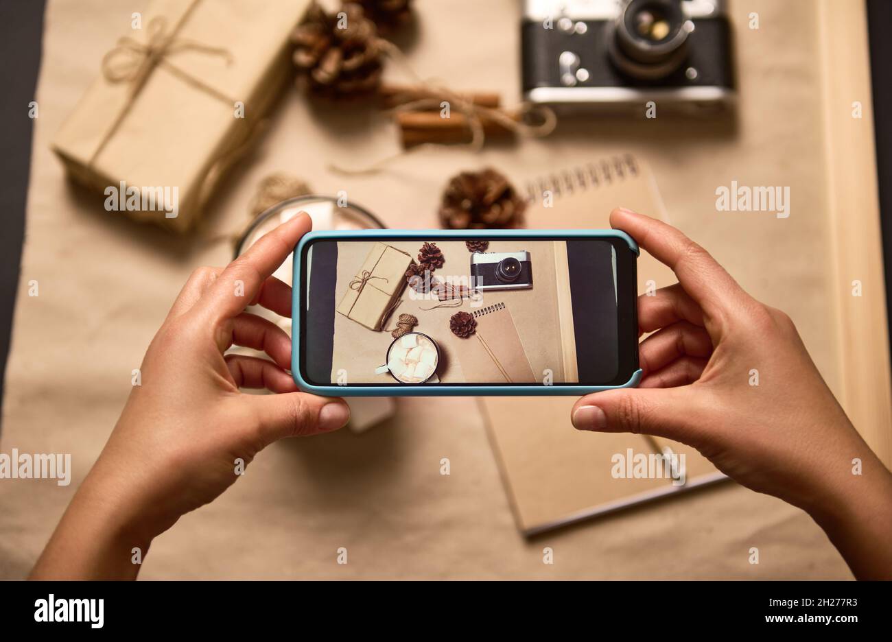 Human hands holding smartphone in live view mode and taking a photo of Christmas composition of cup with cocoa and marshmallows, vintage camera, craft Stock Photo