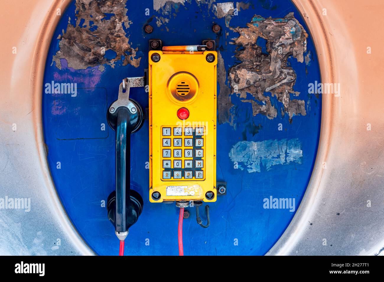 Old, rusted blue telephone booth with old yellow phone inside. Stock Photo