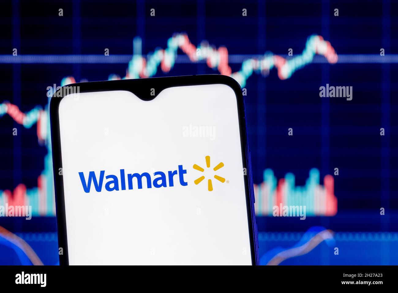 Walmart is an American multinational retail corporation. Smartphone with Walmart logo on the background of the stock chart. Stock Photo