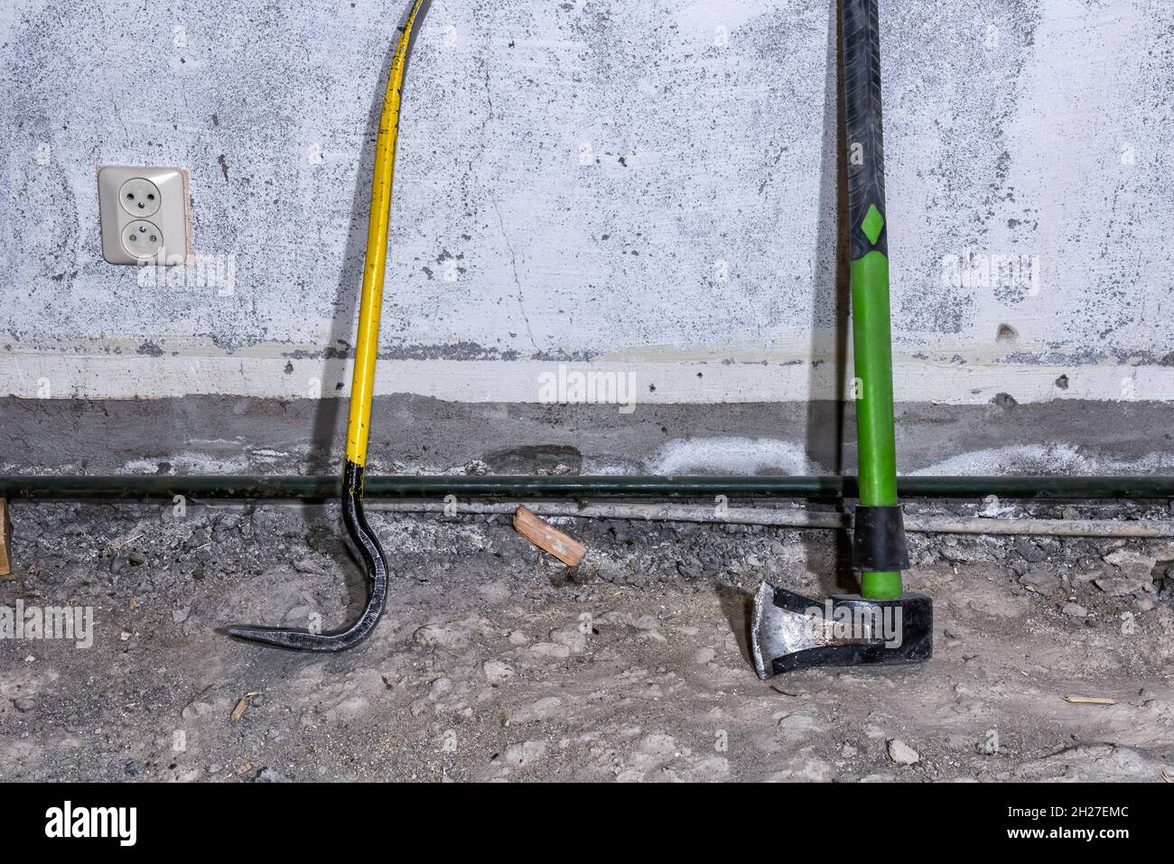 Crowbar and wood splitting maul stand at concrete wall on demolished room floor, close up view Stock Photo