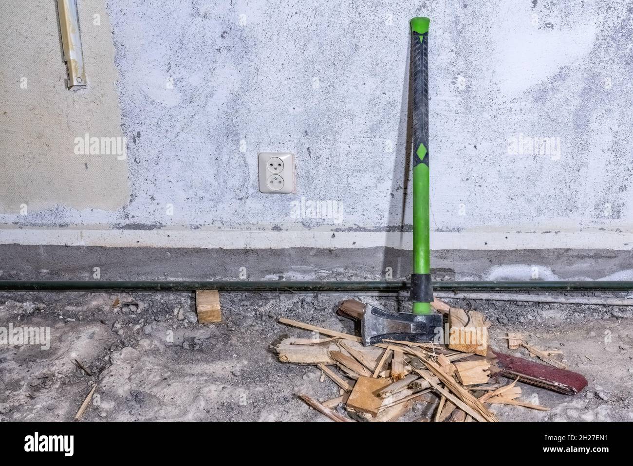 Wood splitting maul stands at concrete wall on demolished room floor, close up view, construction waste debris Stock Photo
